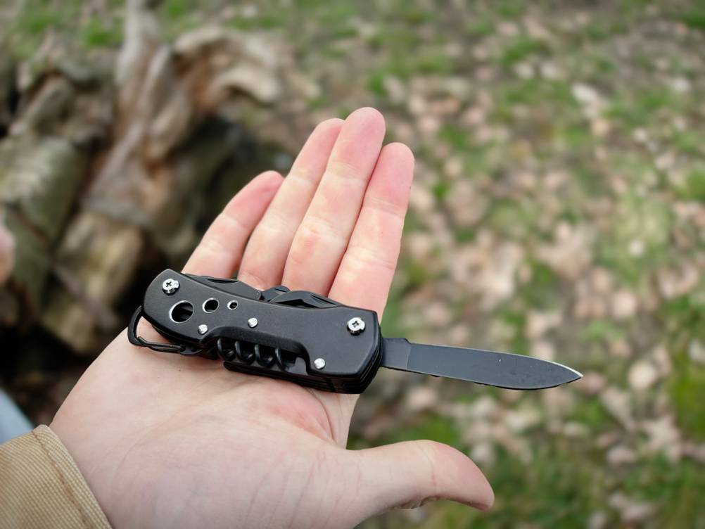 Das Amazon Basics Taschenmesser liegt geöffnet auf einer Handfläche. Die Klinge ist ausgeklappt, der Griff zeigt die schwarzen Metallelemente.