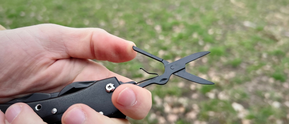 Das Amazon Basics Multitool Taschenmesser wird mit geöffneter Scherenfunktion in einer Hand gehalten. Die kleine Metallschere ist vollständig ausgeklappt.