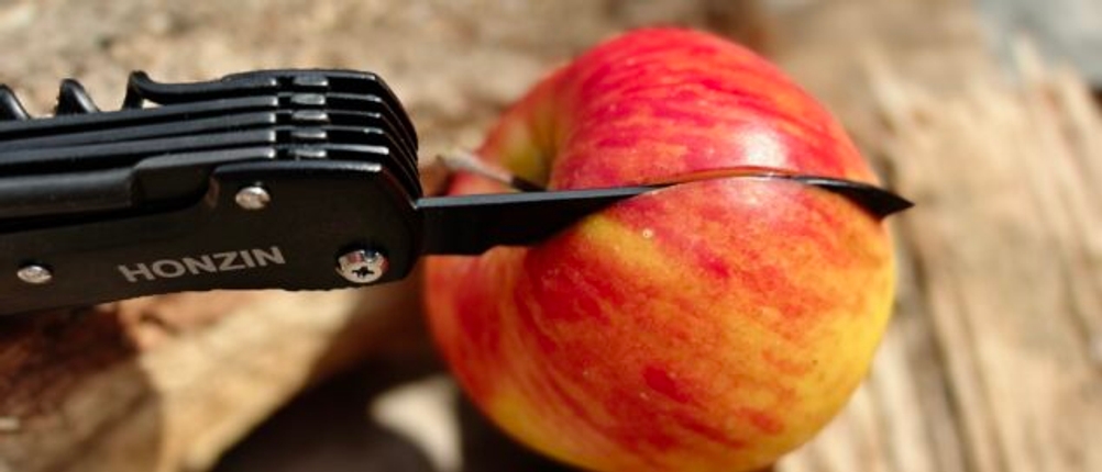Das Honzin Taschenmesser HJ-011 schneidet durch einen Apfel. Die Klinge ist leicht gebogen und in Nahaufnahme zu sehen.