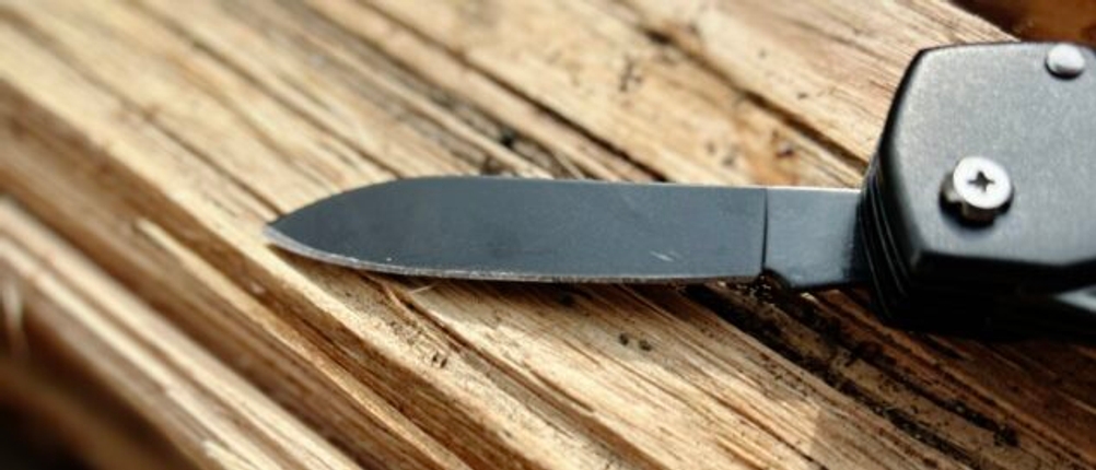 Das Honzin Taschenmesser HJ-011 liegt mit geöffneter Klinge auf hellem Holz. Der schwarze Klingenschliff hebt sich vom Untergrund ab.