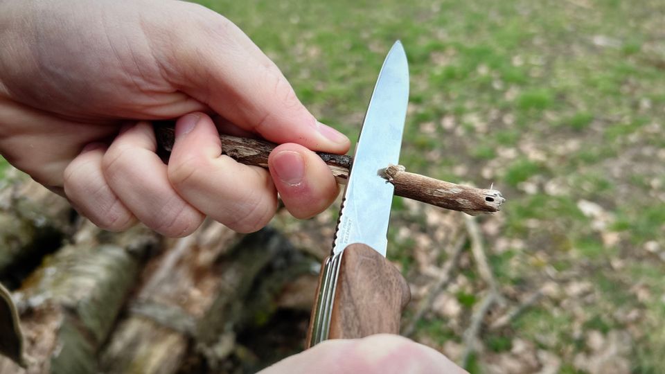 Die Klinge des Victorinox Ranger Wood 55 wird zum Schneiden eines kleinen Holzstocks verwendet. Beide Hände führen das Messer.