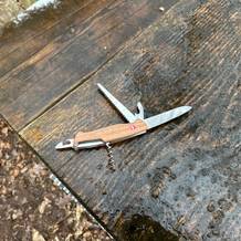 Das Victorinox Ranger Wood 55 liegt geöffnet auf einem nassen Holztisch im Wald. Mehrere Werkzeuge sind ausgeklappt sichtbar.