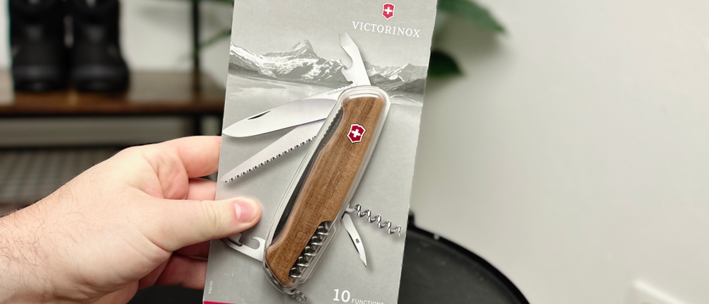 Das Victorinox Ranger Wood 55 ist originalverpackt zu sehen. Eine Hand hält das Produkt vor einem Regal im Innenraum.