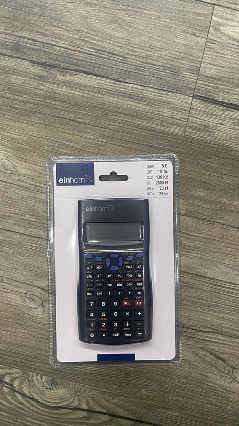 Der getestete Taschenrechner (nicht programmierbar) in Originalverpackung auf einem Holzboden liegend.