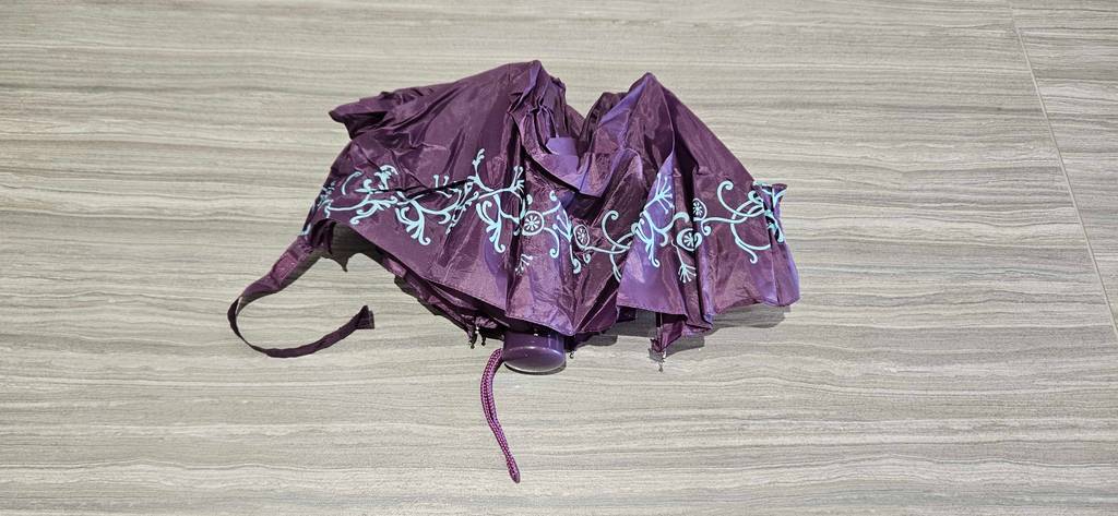 Ein halb ausgebreiteter Taschenschirm liegt zum testen auf einem Laminatboden.