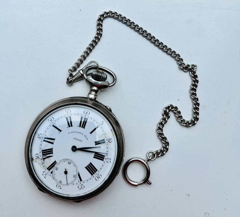 Taschenuhr im Test: Eine Uhr mit weißem Ziffernblatt und einer Kette auf einer weißen Oberfläche liegend.