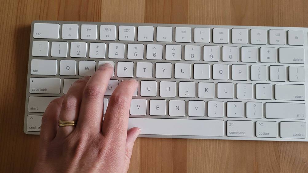 Die Tasten der Apple-Magic-Tastatur im Vergleich mit einer Hand, die darauf liegt
