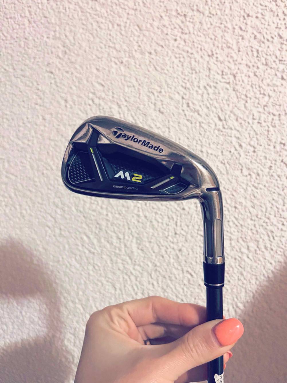 Golfschläger im Test: Hand hält Eisen inklusive Markenzeichen von TaylorMade M2 vor weißer Rauputzfläche.