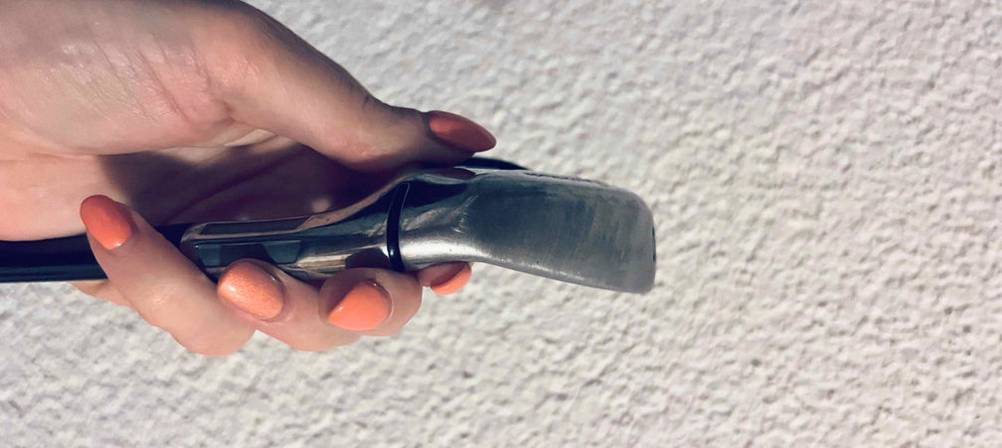 Golfschläger-Test: Hand hält Eisen eines Golfschlägers vor weißer Rauputzwand.