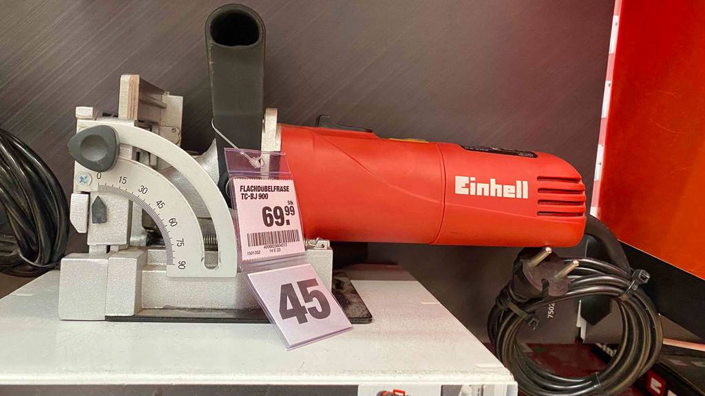 Eine rote Einhell Flachdübelfräse im Test steht inklusive Preisschild, mit Fokus auf den integrierten Winkelanschlag und das aufgerollte schwarze Kabel, in einem Ausstellungsbereich.