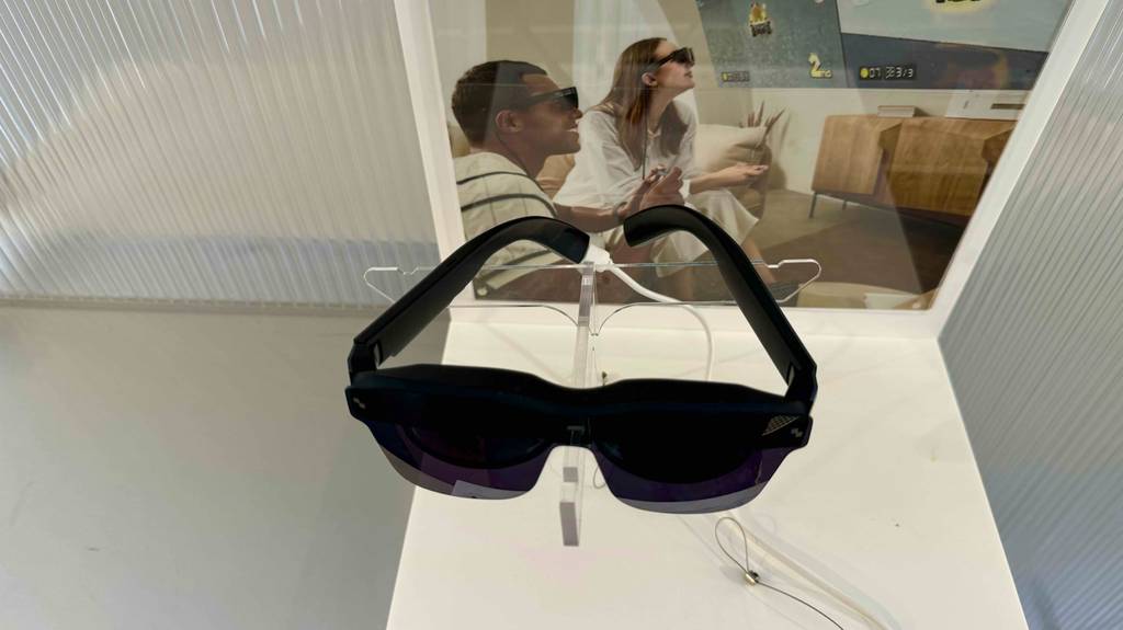 Ansicht von oben auf eine Videobrille im Test, die in einem Geschäft vor einem Plakat mit Videobrillenträgern ausgestellt ist.