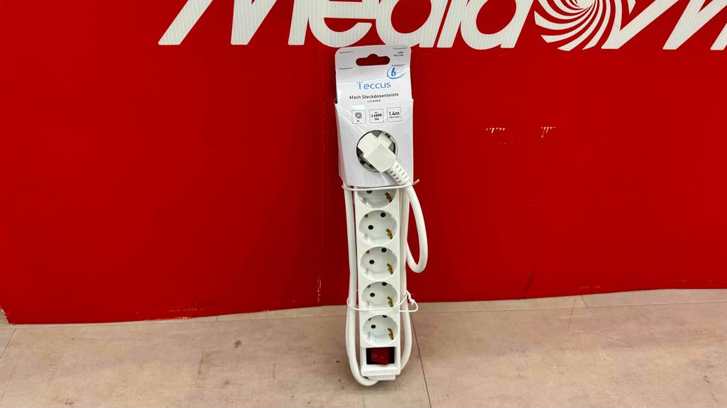 Eine getestete 6-Fach-Steckdosenleiste lehnt bei Media World an einer roten Wand.