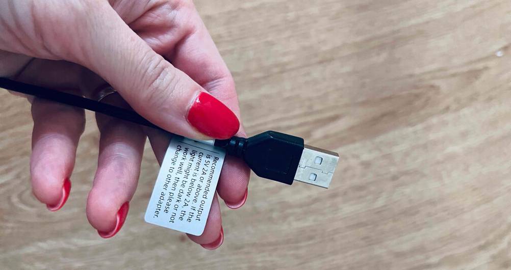 Eine Hand hält den USB-Stecker eines getesteten Ringlichtes vor eine hellbraune Fläche.