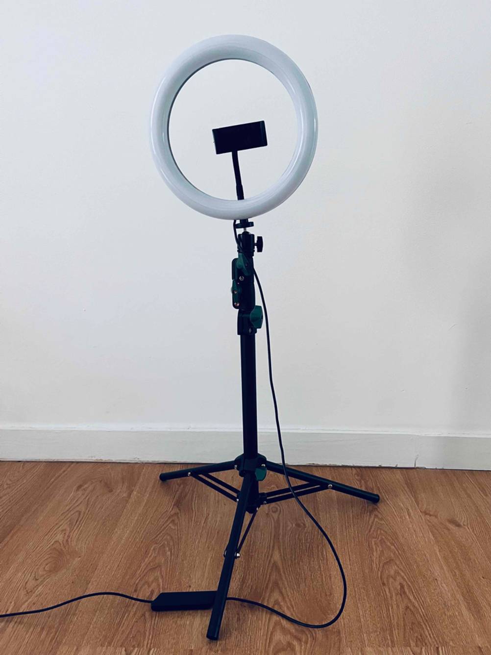 Im Test: Ein Ringlicht mit Ständer und Handyhalterung auf einem Holzboden vor einem hellen Hintergrund.