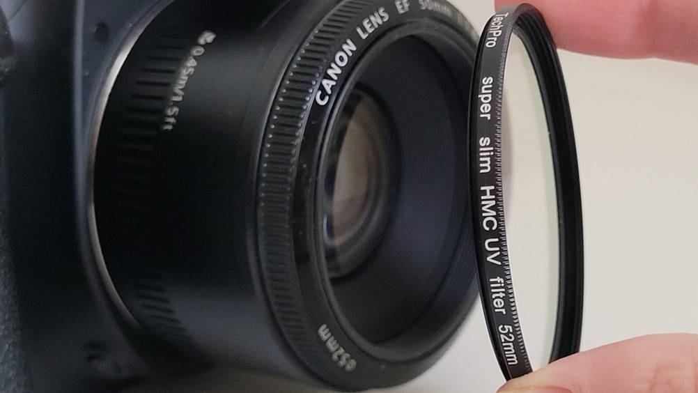 UV-Filter getestet: Eine Hand hält einen Filter vor die Linse eines Objektives.