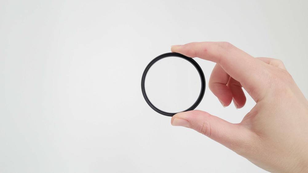 Eine Hand hält einen getesteten UV-Filter zwischen Zeigefinger und Daumen vor einen hellen Hintergrund.