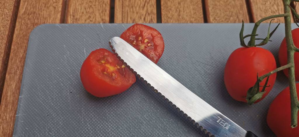 tomatenmessser-test: Detailansicht der gezahnten Klinge eines getesteten Tomatenmessers, die auf einer aufgeschnittenen Tomate liegt.