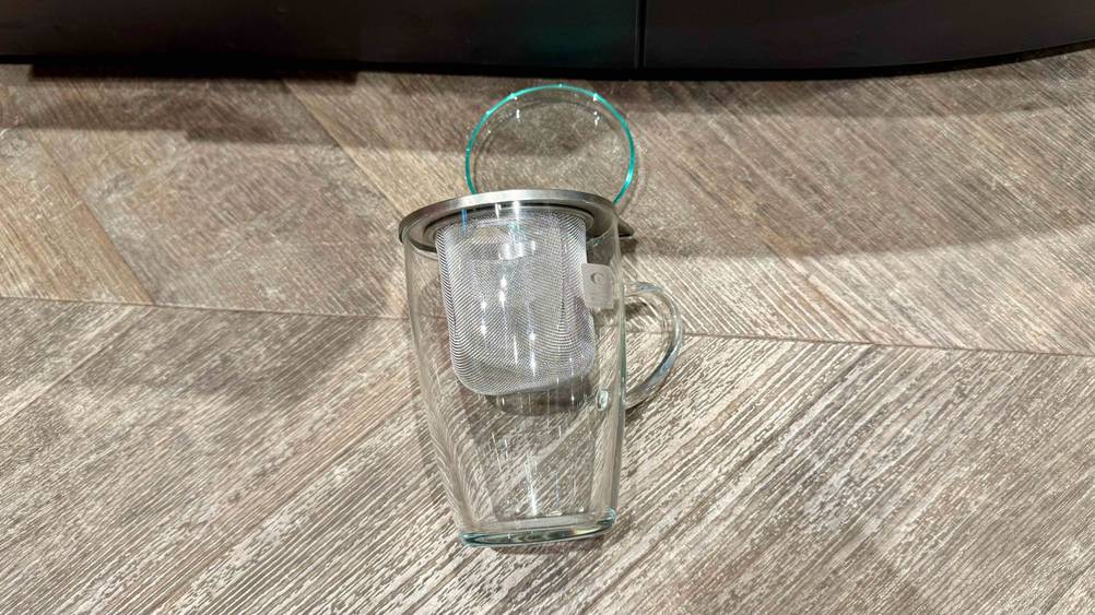 Auf einem Holzboden liegt ein getestetes Teeglas.