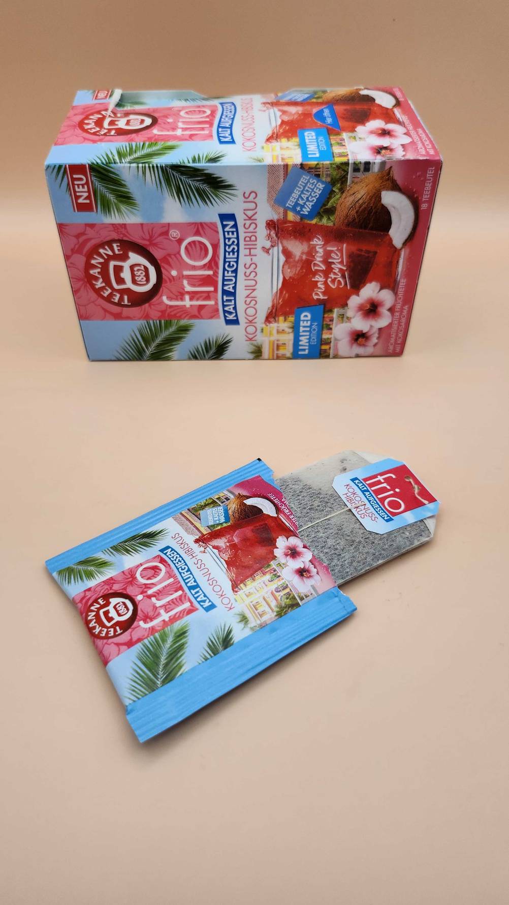 Cold brew Tee getestet: Vor einer Verpackung liegt ein ausgepackter Teebeutel auf einer beigefarbenen Oberfläche.