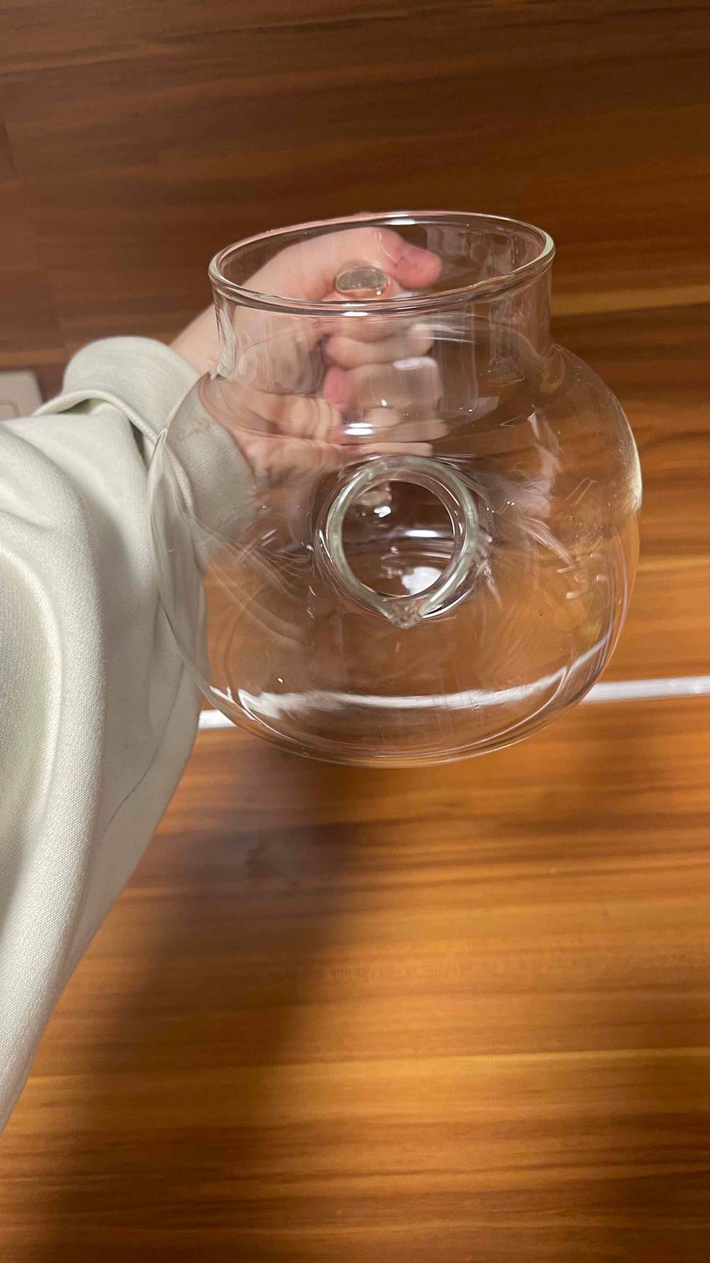 Eine Hand hält eine getestete Teekanne aus Glas mit der Öffnung nach vorn.
