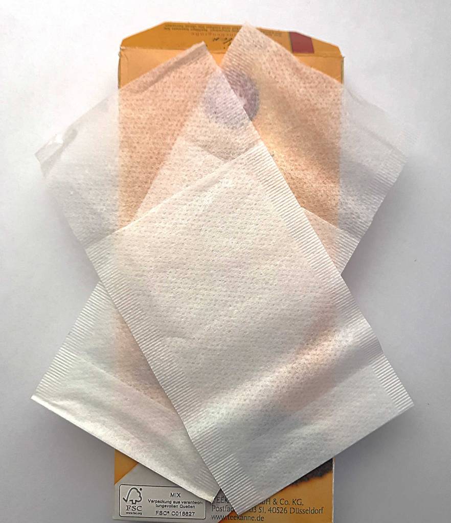 Zwei semitransparente getestete Teebeutel befinden sich auf einer gelben Verpackung.