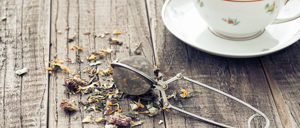 ein Teesieb neben einer Tasse Tee