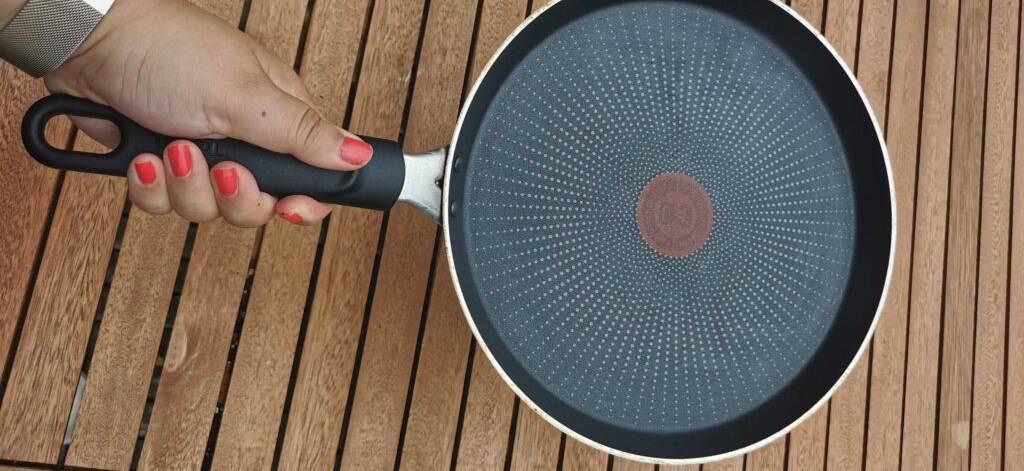 Hand hält eine getestete Pfanne für Crêpes über einem Holztisch.