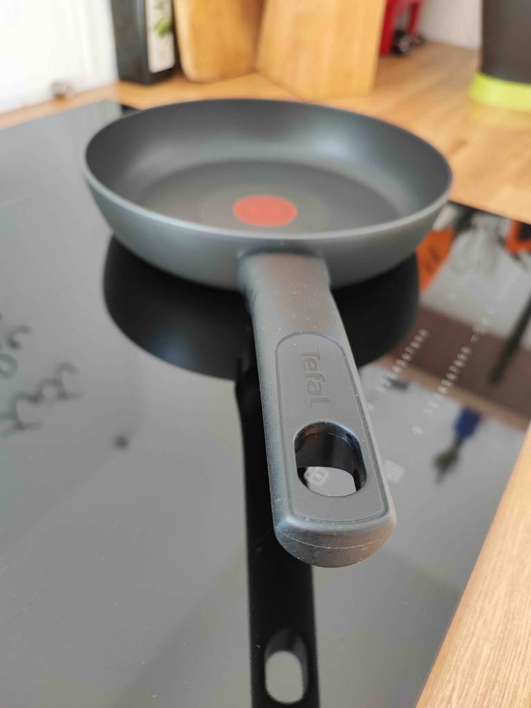 Induktionspfannen-Test: ein schwarzes Modell der Marke Tefal, inklusive Kunststoffgriff mit Aufhänger, steht auf einem ausgeschalteten Induktionsherd.