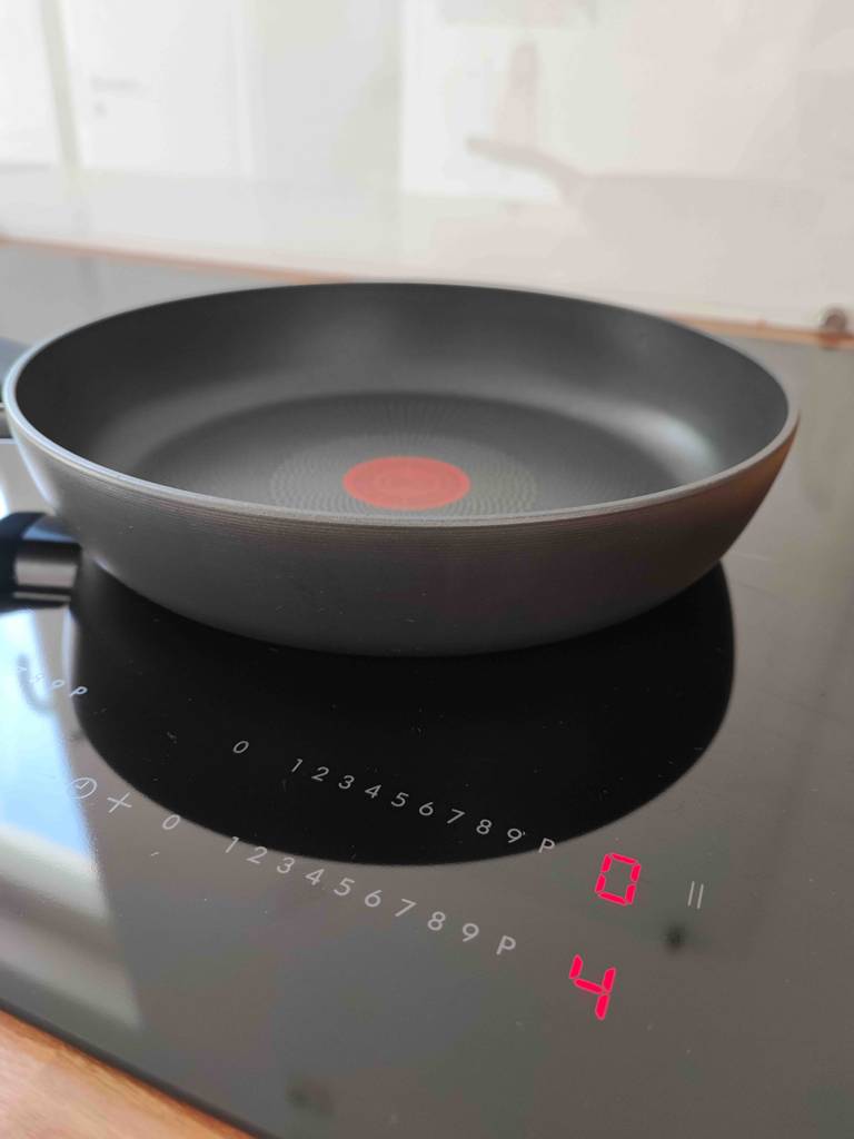 Induktionspfannen im Test: ein schwarzes Modell mit rotem, mittigem Punkt innerhalb der Pfanne steht auf einem eingeschalteten Herd.