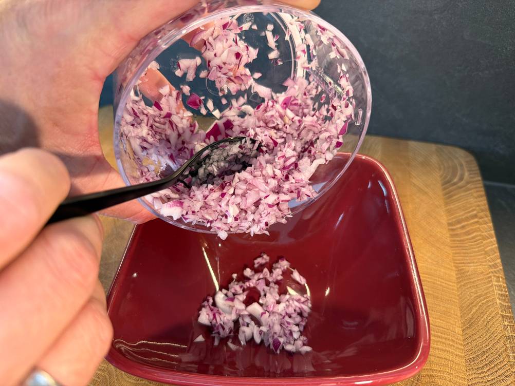 Mit einem Löffel werden Zwiebelstücke aus dem Behälter des Tefal K13304 entfernt.