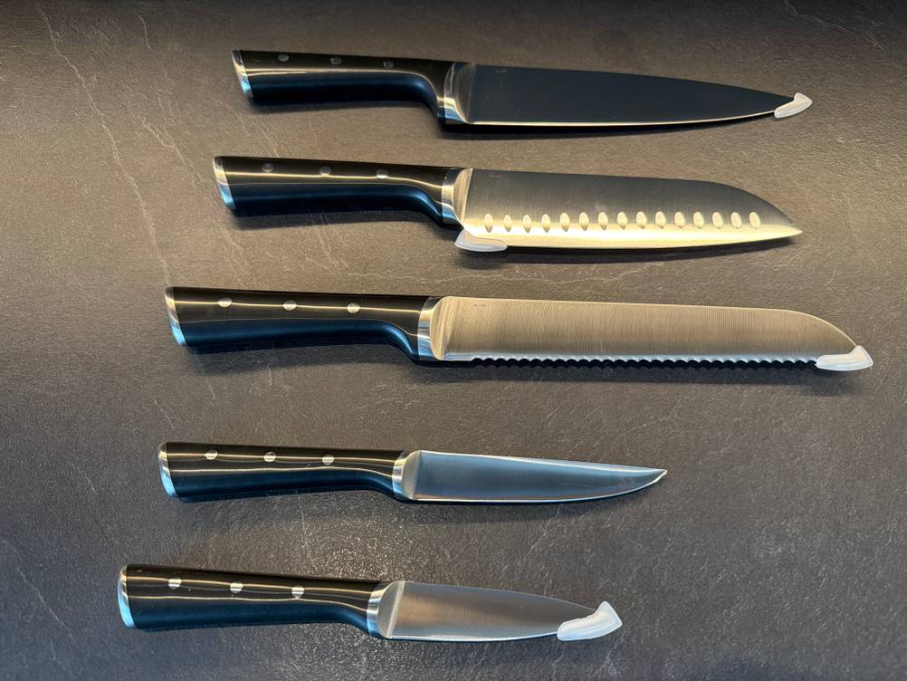 Alle Messer aus dem Messerset Tefal K232S574 liegen auf einer Küchenarbeitsplatte.