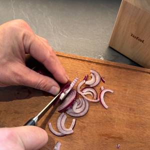 Eine Zwiebel wird mit einem Messer vom Tefal K232S574 geschnitten.