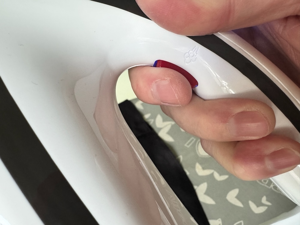 Der rote Knopf an dem Tefal-Dampfbügeleisen wird gedrückt.