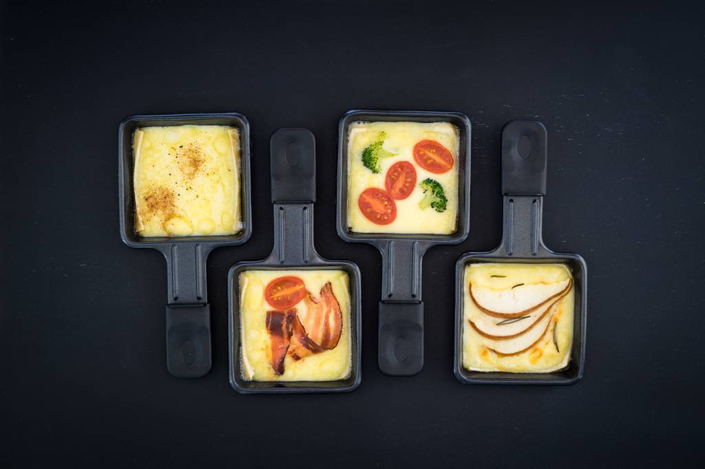 Tefal-Raclette-Test: vier kleine Raclette-Pfännchen sind mit geschmolzenem Käse und Gemüse sowie Schinken gefüllt.