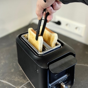 Eine Person nimmt mit einer Zange fertiges Toast aus dem getesteten Toaster von Tefal.