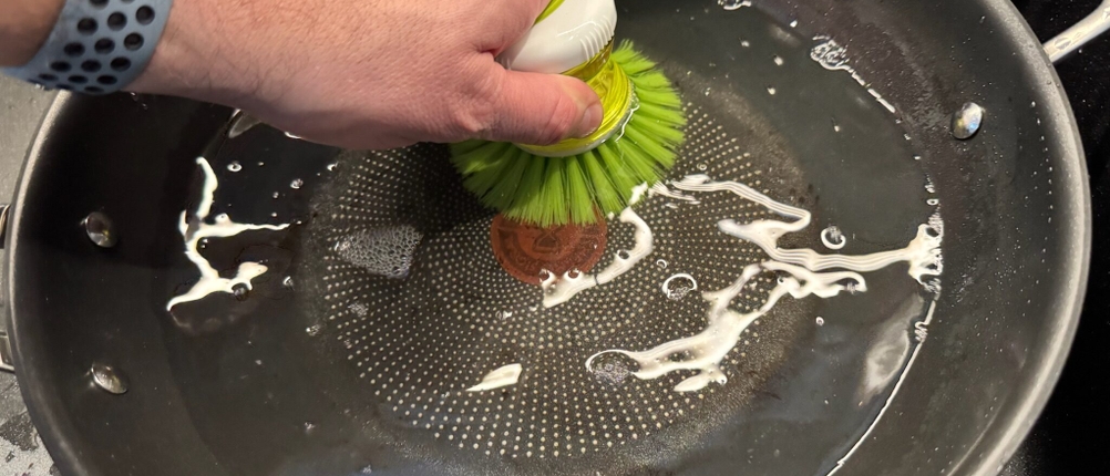 Reinigung der Tefal-Wokpfanne Jamie Oliver Cook's Classic mit einer grünen Bürste