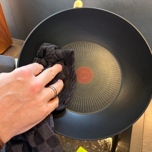 Eine Hand trocknet die Tefal-Wokpfanne Unlimited On mit einem Handtuch ab