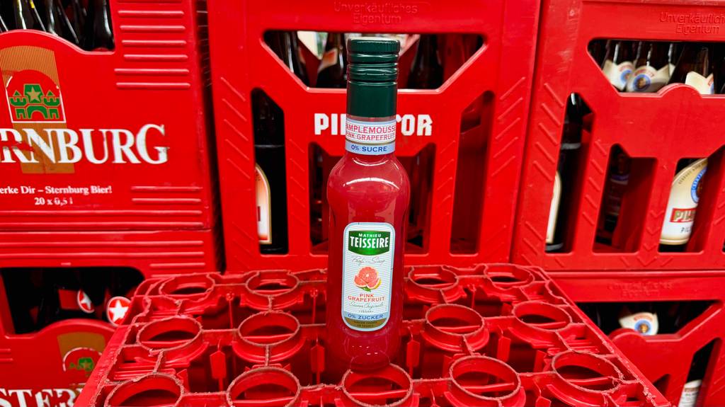Im Test: Fruchtsirup Pink Grapefruit in der Flasche steht auf einem roten Getränkekasten.