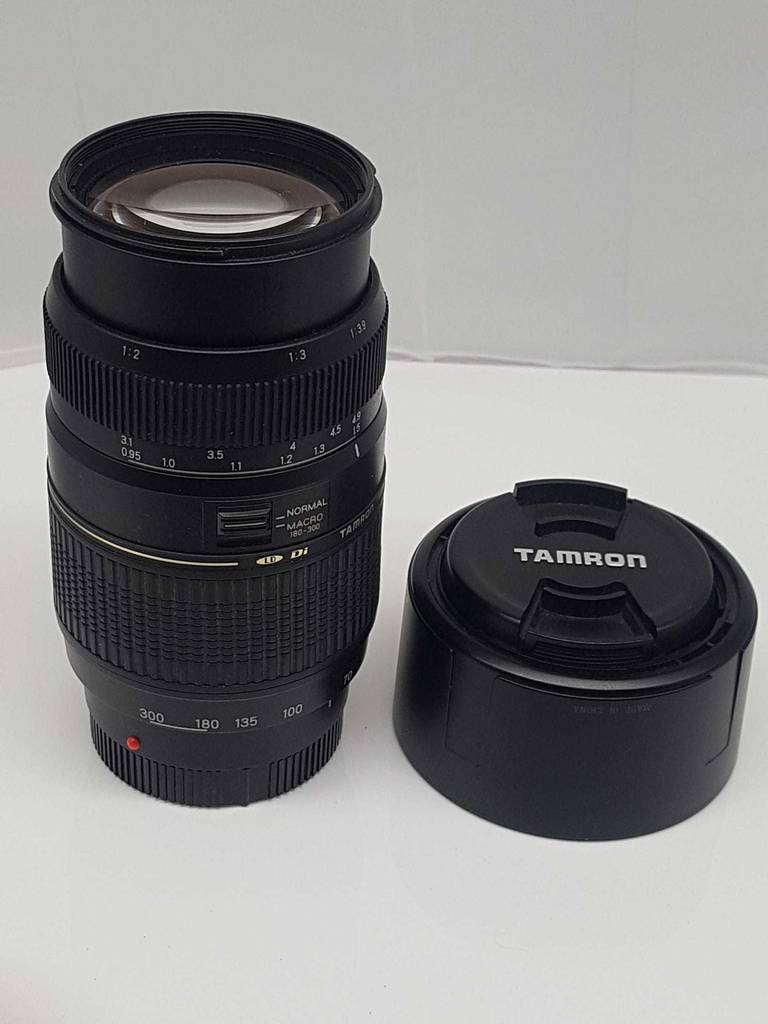 Gesamtansicht von einem stehenden Tamron Teleobjektiv im Test inklusive Objektivdeckel, mit Fokus auf die Linse und die Macro-Funktion.
