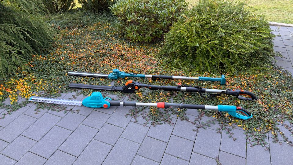 Drei Teleskop-Heckenscheren liegen nebeneinander auf gepflasterten Steinen.