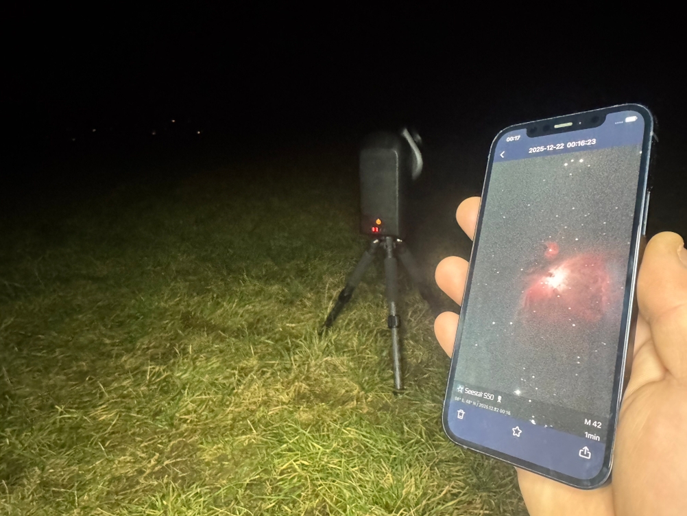 Eine Person hält ein Smartphone mit dem Orionnebel darauf vor das ZWO-Teleskop im Test.