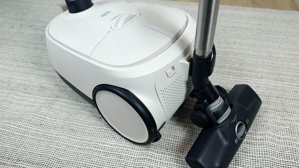 Obenansicht des AEG AB61H6SW Staubsaugers mit schwarzem Schlauch, Bodendüse und Bedienelementen. Der Staubsauger steht auf einem Teppich.