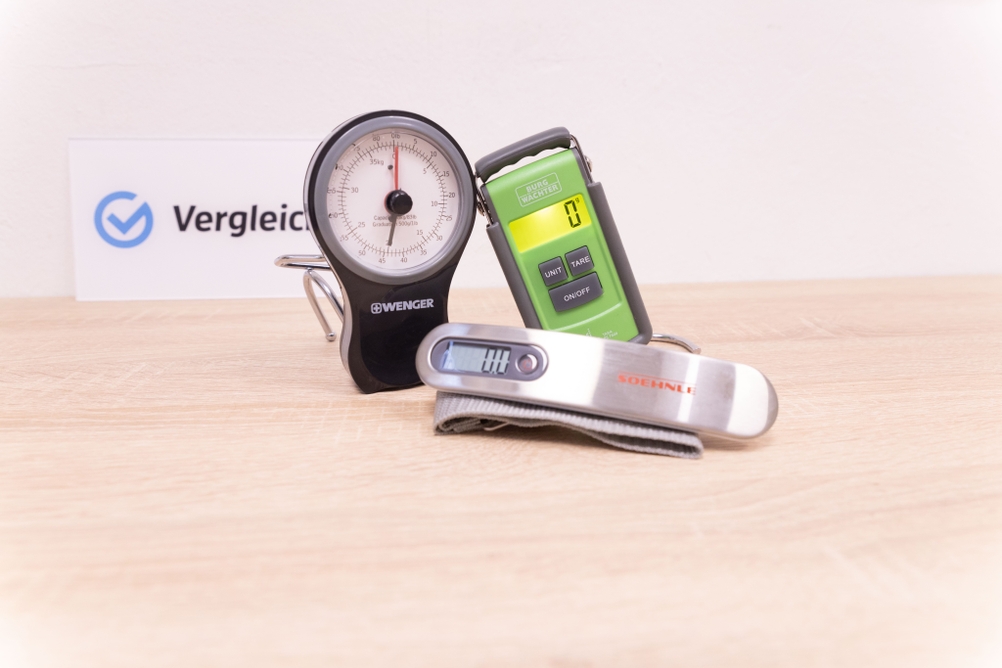 Drei Kofferwaagen liegen auf einem braunen Holztisch.