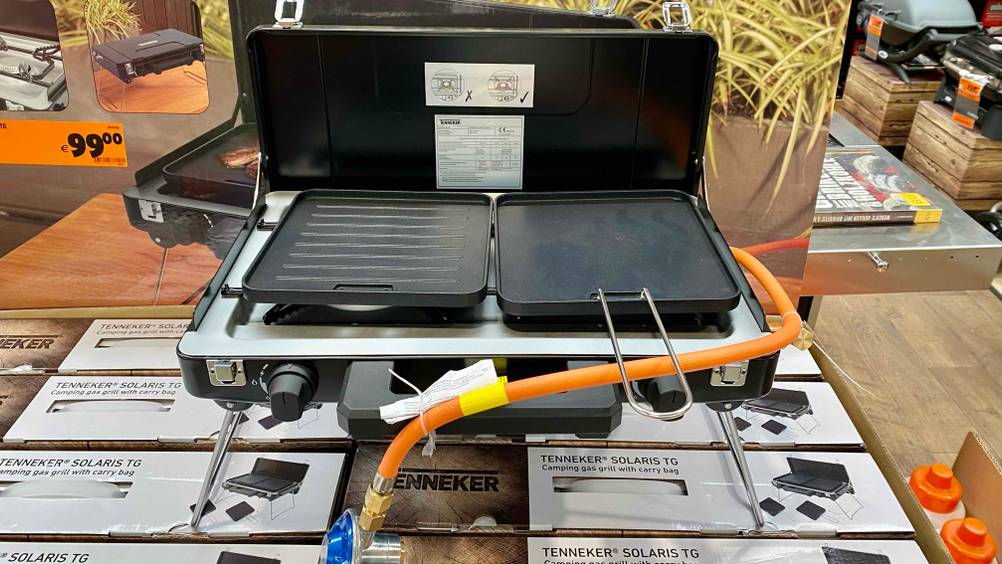 Camping-Gasgrill getestet: Ein Gerät aufgeklappt mit zwei Rosten auf mehreren Kartonagen stehend.