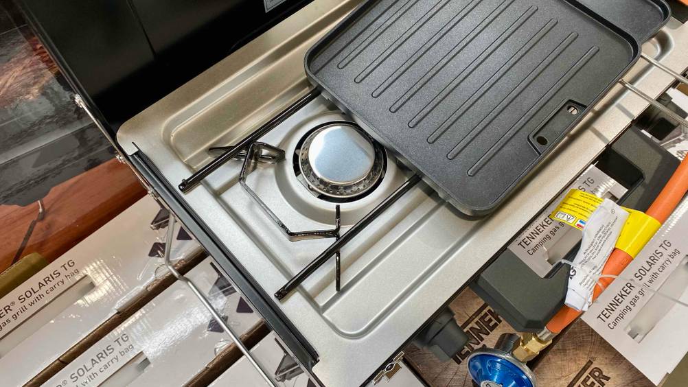 Nahaufnahme des Gasbrenners eines getesteten Camping-Gasgrills, daneben ein Rost.