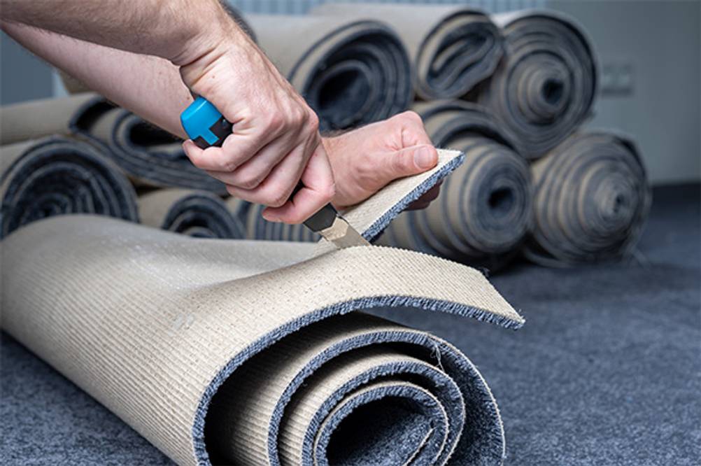 Teppichmesser im Test: Jemand schneidet einen Teppich mit einem blauen Messer zu.