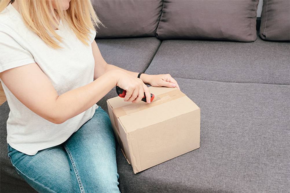 Teppichmesser im Test: Eine Frau, die mit einem Teppichmesser ein Paket öffnet.