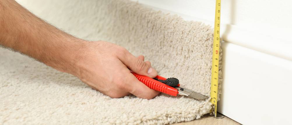 Teppichmesser im Test: Ein Teppichverleger nimmt Maß und schneidet mit dem Teppichmesser den Teppich ab.