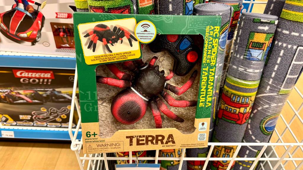 Die ferngesteuerte Spinne im Test steht inklusive Verpackung auf einem Korb mit Spielteppichen.
