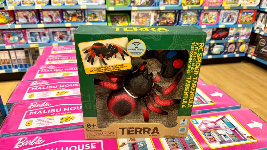 Die getestete ferngesteuerte Spinne steht innerhalb der Verpackung auf mehreren Barbie-Sets in einem Spielzeuggeschäft.